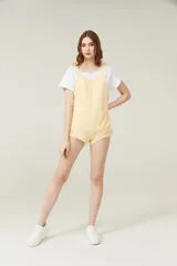 Mono corto color amarillo pastel, con breteles finos que se atan en los hombros, escote recto y dos bolsillos delanteros.