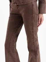 Pantalón de mezclilla marrón chocolate, de tiro medio y corte flare con perneras ligeramente acampanadas y costuras verticales decorativas en el frente.
