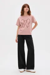 Remera de algodón color rosado, de manga corta y cuello redondo, con diseño frontal de un moño grande confeccionado con lentejuelas.