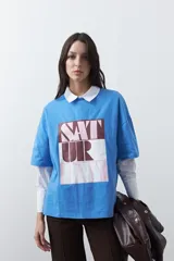 Remera de corte boxy fit color azul, con estampa frontal rectangular que contiene la palabra 'SATURDAY' en tonos marrón y rosado. Presenta un diseño de silueta amplia y caída relajada.