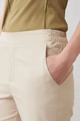 Pantalón de corte recto y tiro medio, confeccionado en tela de gabardina color beige. Presenta cierre frontal con cremallera y botón oculto, bolsillos laterales y costuras verticales decorativas en la parte superior.