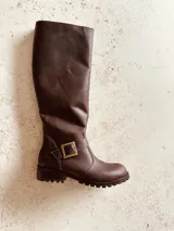 Bota de caña alta color marrón de cuero, con hebilla dorada y suela track.