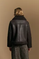 Campera tipo gamulán de cuero sintético negro, con interior y detalles de corderito sintético al tono en cuello y ruedo. Presenta cierre frontal metálico y diseño de silueta relajada.