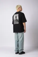 Remera negra de corte oversize con cuello redondo y estampa pequeña en el centro del pecho con forma de ojo que contiene un símbolo de yin y yang.