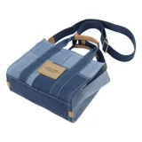 Bolso tipo tote de Marc Jacobs, modelo Mini Traveler, confeccionado en denim con diseño de patchwork en diferentes tonos de azul. Presenta el logo de la marca estampado en el frente, doble asa superior y correa de hombro ajustable y extraíble en color azul marino con detalles en cuero tostado.