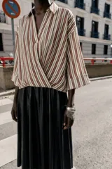 Camisa de cuello solapa con escote en pico, manga tres cuartos con vuelta y bajo asimétrico con pliegues delanteros que generan un efecto abullonado.