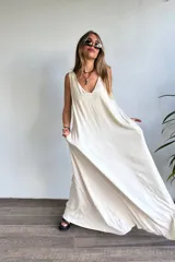 Vestido largo sin mangas, color natural/crudo, con escote en V profundo y corte holgado. Presenta aberturas laterales en la falda.