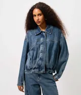 Campera de jean azul con pliegues frontales y posteriores, cuello clásico, cierre frontal embutido y mangas largas. Presenta un diseño de silueta levemente ajustada con terminaciones simples en puños y bajo.
