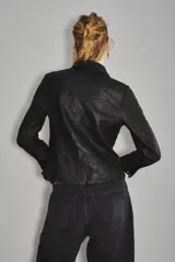 Camisa de cuero ovino con cierre frontal de botones metálicos a presión, cuello clásico y bolsillos delanteros. Presenta un diseño de manga larga con puños abotonados.
