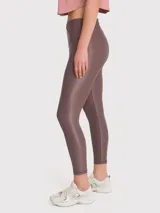 Calza deportiva de tiro alto con cintura en forma de V, confeccionada en tela brillante con acabado efecto cuero. Presenta un diseño ajustado de largo al tobillo.
