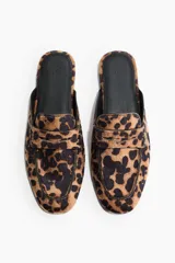 Mules estilo mocasín con punta redonda, modelo penny con costura tradicional en el empeine, forro interior negro y exterior con estampado animal print de leopardo.