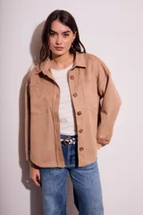 Sobrecamisa de mujer color camel, de estilo shacket, confeccionada en tejido de gamuza sintética. Presenta cuello camisero, botones frontales marrones y dos bolsillos de parche con tapa en el pecho. El calce es oversize.