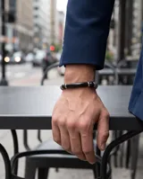 Pulsera masculina compuesta por una barra central de piedra onix negra, flanqueada por piezas de acero con textura grabada y esferas metálicas. Diseño elegante y moderno con cierre ajustable.