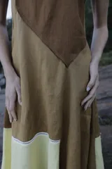 Vestido midi de lino color salmón, de corte amplio y silueta holgada. Presenta diseño con cortes irregulares y detalles de pasamanería en el escote y costuras. Cuenta con breteles dobles tipo cuerda y ruedo asimétrico.