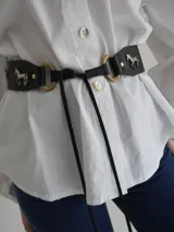 Cinto ancho de cuero marrón con apliques metálicos decorativos en forma de sol, caballo y herraduras, acompañado de tachas.