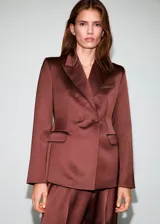 Blazer de corte recto y diseño estructurado, confeccionado en tejido satinado color marrón. Presenta cuello con solapas de muesca, cierre frontal de doble botonadura, bolsillos de solapa en el frente y bolsillo de parche en el pecho. Incluye forro interior y mangas largas con puños abotonados.