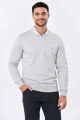 Buzo tejido de algodón color gris melange, de diseño clásico con escote en V, mangas largas y puños y ruedo acanalados. Cuenta con un pequeño bordado en el pecho.
