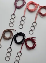 Gargantilla tipo choker confeccionada en cordón de símil gamuza negro, con dije colgante compuesto por tres argollas metálicas plateadas entrelazadas.