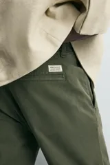 Pantalón chino de corte ajustado, color beige, con bolsillos laterales y bolsillos traseros de vivo. Cuenta con cierre frontal de cremallera y botón.