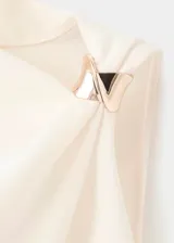 Blusa sin mangas de color crema con cuello redondo y diseño asimétrico. Presenta un detalle metálico en uno de los tirantes, fruncido lateral y cierre de cremallera en la parte posterior.
