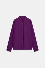 Camisa de manga larga en color violeta, con cuello solapa y cierre frontal de botones. Presenta un diseño de corte recto con detalle de pliegues en la espalda.