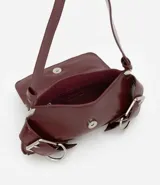 Cartera tipo baguette de tamaño pequeño, confeccionada en poliuretano color negro. Presenta una solapa frontal con detalles de hebillas metálicas decorativas en los laterales y un asa de hombro ajustable.