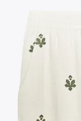 Pantalón color crema de tiro medio con cintura elástica ajustable y bolsillos delanteros. Presenta bordados florales en negro y corte ancho.