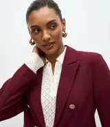 Blazer de sastrería color bordó, de corte slim, con solapas clásicas, cierre frontal cruzado con botones dorados y bolsillos laterales con solapa.