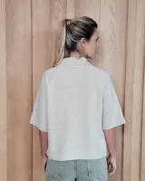 Cardigan de punto color arena, con cuello camisero, cierre frontal de botones y mangas cortas con terminación acanalada. Presenta dos bolsillos frontales tipo parche.