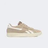 Championes Reebok modelo Court Retro, confeccionados en gamuza color beige con detalles en blanco y suela de goma color marfil. Presentan el logo de la marca en el lateral y en el talón.