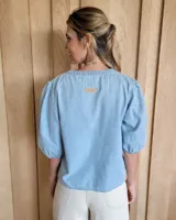 Blusa celeste de mangas 3/4 abullonadas, escote en V con detalle de bordado y lazo decorativo.