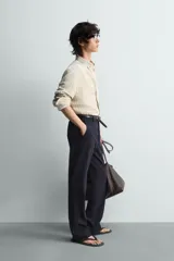 Camisa de algodón de corte relajado, con cuello solapa abotonado (button-down) y manga larga terminada en puño con botón. Presenta un patrón de rayas verticales finas en tonos beige claro y marrón/verde oliva.