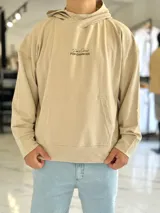 Canguro oversize color beige, con capucha y amplio estampado tipográfico en la espalda.