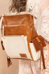 Mochila de cuero color marrón con textura croco y detalles en cuero color beige. Tiene múltiples bolsillos externos con cierre y flecos laterales.