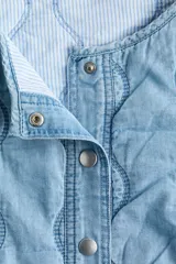 Campera acolchada ligera de denim en mezcla de algodón y lyocell, modelo Divided de H&M. Presenta cuello redondo, cierre frontal con botones a presión, hombros ligeramente caídos, mangas abullonadas y elástico revestido en los puños y el dobladillo inferior. Diseño pespunteado con ondas.