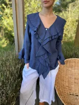 Camisa de lino azul marino con volados en cascada a lo largo del frente y en los puños de las mangas largas. Presenta un escote en V con un botón de nácar visible.