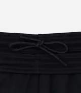 Pantalón deportivo de corte slim para hombre, confeccionado en poliéster color negro. Presenta cintura elástica con cordón de ajuste, bolsillos laterales y diseño ajustado en muslos y rodillas.