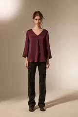 Blusa de satén color bordó con cuello en V y mangas tres cuartos. Presenta un diseño holgado con un pliegue central en el frente.