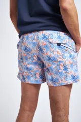 Short de baño con estampado tropical de piñas y hojas en tonos azules sobre fondo rosado. Cuenta con cintura elástica con cordón ajustable, bolsillos laterales, un bolsillo trasero y suspensor interno.