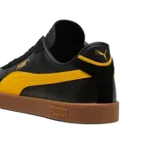 Championes Puma modelo Club Li Era, con diseño de perfil bajo en color negro, franja lateral blanca característica de la marca y suela de goma color caramelo. Presenta detalles en dorado en el logo lateral y la lengüeta.