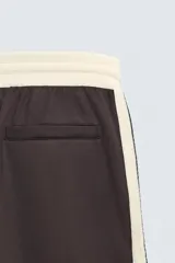 Pantalón jogger de corte wide fit en tejido compacto color gris oscuro. Presenta cintura elástica con cordón ajustable, bandas laterales en contraste color beige y costuras frontales tipo pinza.