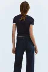 Jean de denim azul oscuro, de tiro alto y piernas amplias con pliegues frontales y traseros. Cuenta con cierre y doble botón metálico en la cintura.