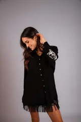 Camisa beige de corte amplio, con cuello clásico, cierre frontal con botones, mangas largas con puños abotonados y bordado floral en las mangas.