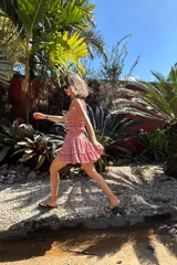 Vestido corto color marrón oscuro, sin mangas y con escote recto. Presenta un cuerpo fruncido con elástico y una falda corta con volados en el ruedo.