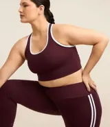 Top deportivo sin copa, color bordó, con escote en U y espalda tipo nadador. Presenta ribetes de color blanco en el contorno del escote y las sisas.