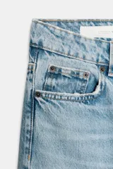 Jeans de mujer, tiro alto, color azul medio con efecto desgastado (lavado claro en muslos y oscuro en bordes). Corte recto y ancho (mom fit) con cinco bolsillos y cierre frontal de botón y cremallera.