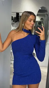 Vestido corto de fiesta color azul eléctrico con acabado brillante. Presenta un diseño asimétrico de un solo hombro con manga larga y cuello tipo choker integrado.