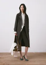 Chaqueta estilo gabardina larga en color gris oscuro, con doble botonadura frontal, solapas clásicas, bolsillos y trabillas ajustables en los puños.