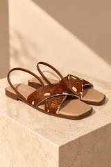 Sandalias planas de cuero con tiras cruzadas de pelo con estampado animal print tipo vaca en tonos marrón y blanco, plantilla beige y tira trasera fina de cuero marrón.
