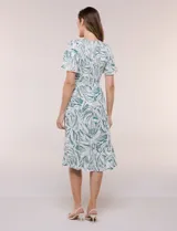 Vestido midi de rayón con estampado de hojas en tonos verde oscuro y blanco. Cuenta con escote en V, pechera fruncida con punto smock, mangas cortas con detalles de pompones en los bordes y lazo ajustable en la cintura.